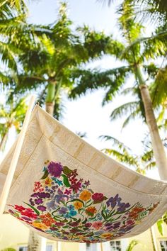 an umbrella is hanging in front of some palm trees and flowers on the outside of it