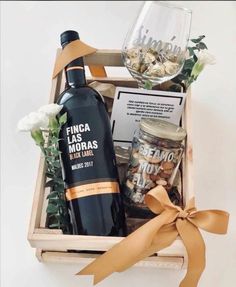 a bottle of wine and some snacks in a box with a ribbon around it on a table