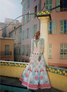 a mannequin dressed in an elaborately designed dress stands on a balcony overlooking the city