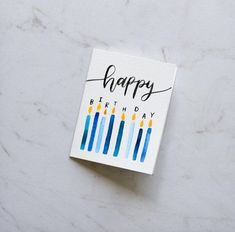 a happy birthday card with blue and yellow candles on it sitting on a marble surface