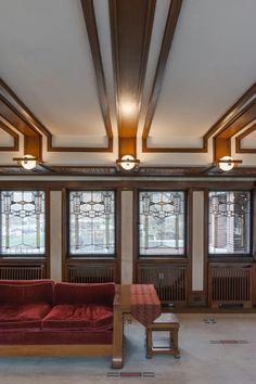 a red couch sitting in the middle of a living room next to two large windows