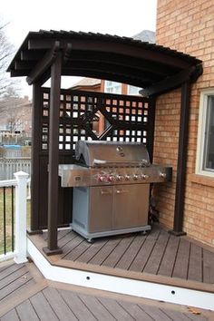 an outdoor grill on a deck next to a brick building with a pergolated roof