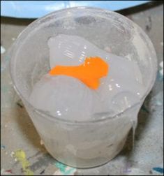 an orange piece of plastic sitting on top of ice in a cup filled with water