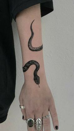 a woman's hand with a snake tattoo on her left arm and two rings around the wrist