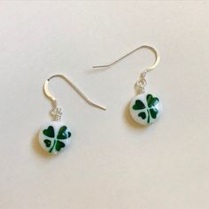 These unique earrings are made of white blown glass. The glass beads each have a beautiful translucent green four leaf clovers on them. They hang from sterling silver ear hooks. These earrings are modest but perfect to wear to show your Irish pride or to wear to celebrate Saint Patrick's Day. These earrings measure one (1) inch in length and are short and sweet. Please note because these beads are handmade, the shamrock on the earrings you receive may look slightly different from the photos. See Clover Shaped Jewelry, Clover Jewelry Four Leaf, 4 Leaf Clover Earrings, Lucky Earrings, Four Leaf Clover Jewelry Vintage, Shamrock Earrings, Four Leaf Clover Charm, Irish Pride, Clover Earrings