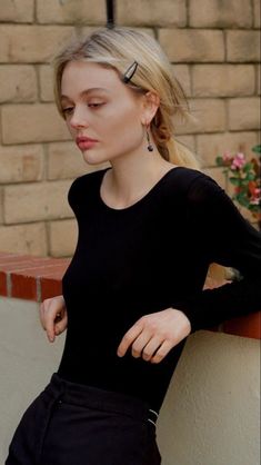 a woman leaning against a brick wall with her hand on her hip and looking down