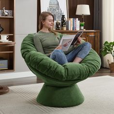 a woman sitting in a green bean bag chair reading a book on the floor next to a coffee table