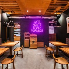 an empty restaurant with wooden tables and chairs in front of a neon sign that reads late nights early mornings