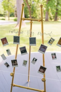 a gold frame with photos hanging from it on a white cloth covered table in front of trees