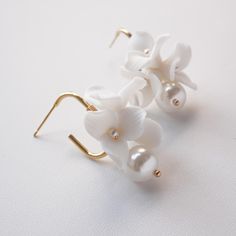 two white flowers are attached to gold earwires on a white surface with pearls