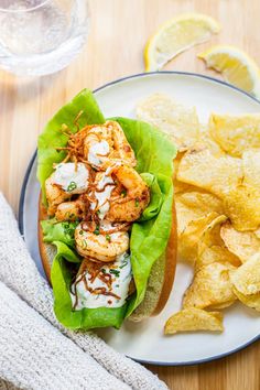 a sandwich with shrimp, lettuce and chips on a plate next to a glass of water