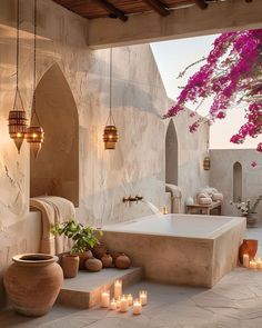 an outdoor bathtub with candles and potted plants on the side, surrounded by stone walls