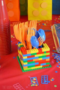 colorful plastic utensils in a lego block holder on a red tablecloth with confetti