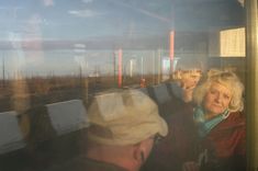 an older woman sitting on a bus looking out the window at something in the distance