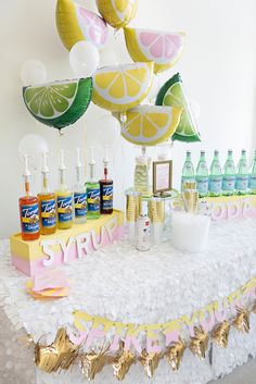 a table topped with lots of lemons and bottles next to balloons in the air