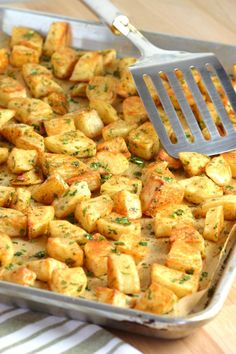 a pan filled with tofu sitting on top of a wooden table next to a spatula