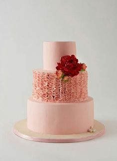 a three tiered cake with pink icing and red flowers