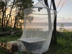 a bathtub in the middle of a field next to some trees and water with a net hanging over it