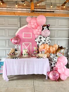 a table topped with lots of balloons and farm animals next to a pink cow house