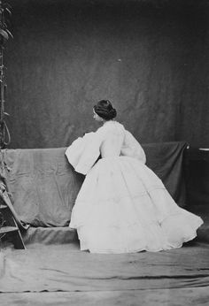 an old black and white photo of a woman in a long dress sitting on a couch