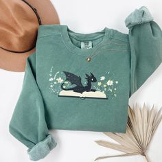 Dragon Book Sweatshirt, Fantasy Sweatshirt, Bookworm sweatshirt, bookish sweatshirt, book club sweatshirt, Book Lover, Book Crewneck Comfort Colors 1566 Sweatshirt  Luxurious comfort and style are what this unisex, garment-dyed sweatshirt is all about. It's made with 80% ring-spun cotton and 20% polyester and the fabric is 3-end garment-dyed, ring-spun, color-blast fleece with a 100% cotton face. Each sweatshirt comes with a relaxed fit, a rolled-forward shoulder, and a back neck patch.  .: 80% ring-spun cotton, 20% polyester .: Medium-heavy fabric (9.5 oz /yd² (322.1 g/m .: Relaxed fit .: Sewn in twill label .: OEKO-TEX certified low-impact dyes Book Lovers Sweatshirt, Styling Oversized Sweatshirts, Book Crewneck, Book Sweatshirts, Bookish Sweatshirts, Bookworm Sweatshirt, Book Outfits, Dragon Book, Cute Crewneck