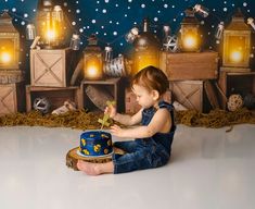 a baby sitting on the floor with a cake in front of him and some lights