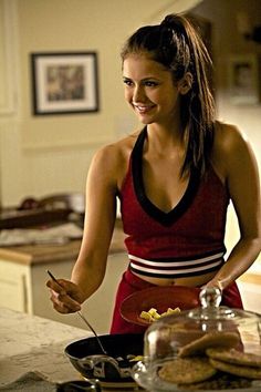 a woman standing in front of a counter holding a knife and fork with food on it