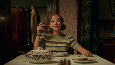 a woman sitting at a table with a teapot and plate in front of her