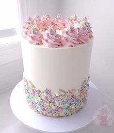 a large white cake with pink frosting and sprinkles on the top