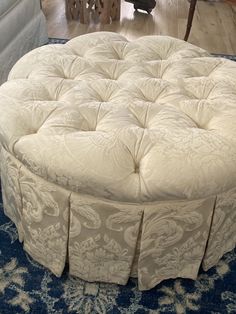 a round ottoman sitting on top of a blue rug in front of a white couch