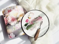 a white plate with pink flowers on it next to a painting brush and paper towel