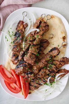 grilled meat with onions and tomatoes on a white plate next to mashed potatoes