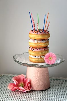 a stack of donuts sitting on top of a cake plate with candles sticking out of them