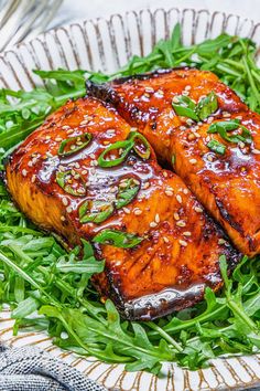 two pieces of grilled salmon sitting on top of green vegetables and garnished with sesame seeds