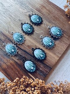 six blue glass cabochons sitting on top of a wooden board next to dried flowers