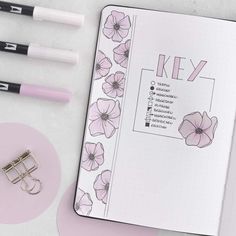 an open planner with pink flowers on it next to some pens and paper clippings