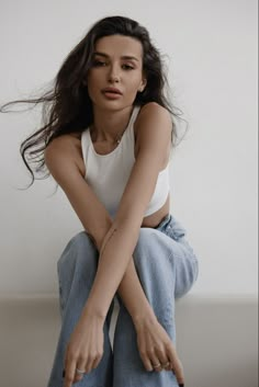 a woman sitting on top of a white couch with her arms crossed and hands behind her back