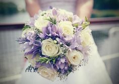 a bride holding a bouquet of white and purple flowers