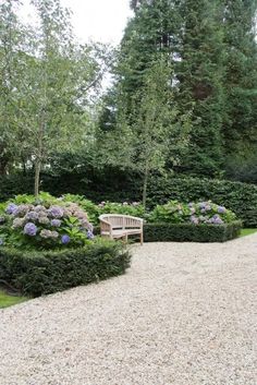 a park bench sitting in the middle of a gravel path surrounded by bushes and trees