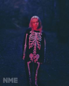 a woman standing in the dark with a skeleton on her chest and arms behind her back