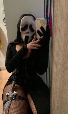 a woman wearing a skeleton mask and holding a cell phone in her hand while sitting on the floor