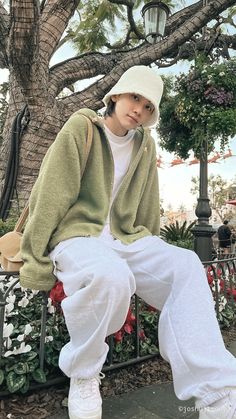 a person sitting on a bench wearing white pants and a green jacket with hoodie