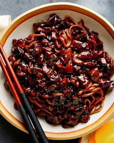 a bowl filled with noodles and sauce next to chopsticks on top of a table