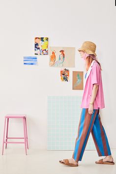 a woman in pink shirt and blue pants walking by a wall with pictures on it