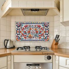 an ornate tile backsplash hangs above the stove top in this white tiled kitchen