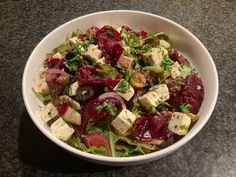 a salad with beets, cheese and lettuce in a white bowl on a table