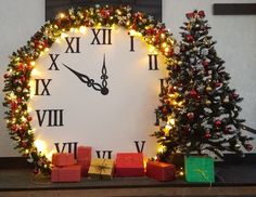 a large clock with christmas decorations and presents on the mantle next to it is lit up