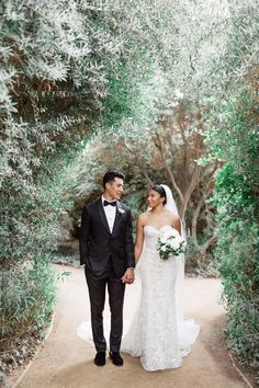 a bride and groom holding hands while walking down a path