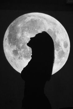 the silhouette of a person standing in front of a full moon