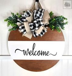 a welcome sign hanging on the side of a door with burlocks and greenery